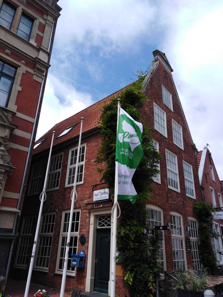 Die grün-weiße Mayors-for-Peace-Flagge weht vor einem roten Backsteingebäude in Leer (Ostfriesland) im Wind.